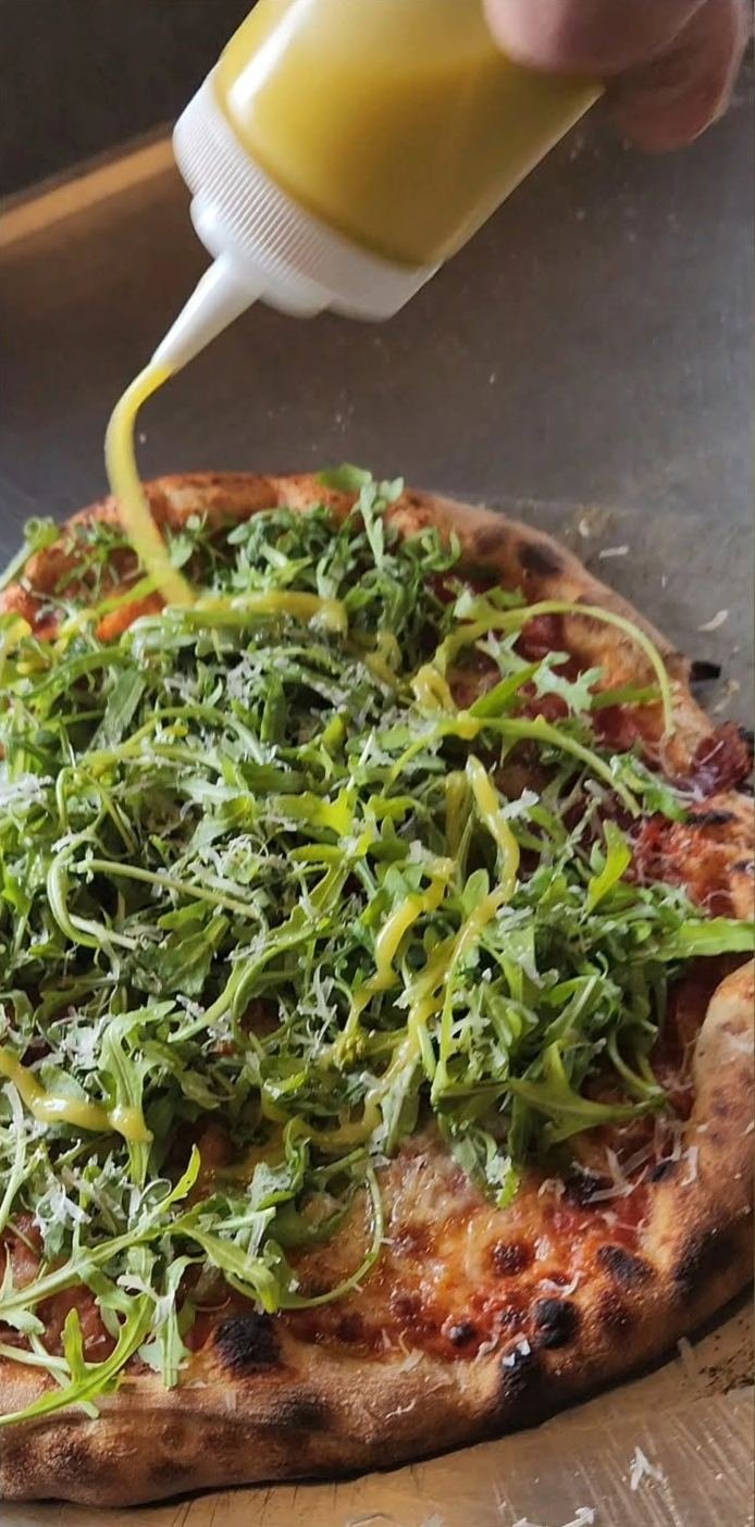 Pizza med rucola og ost bliver dryppet med olie